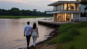young romantic couple holding hands, walking by lake near their modern house, back view